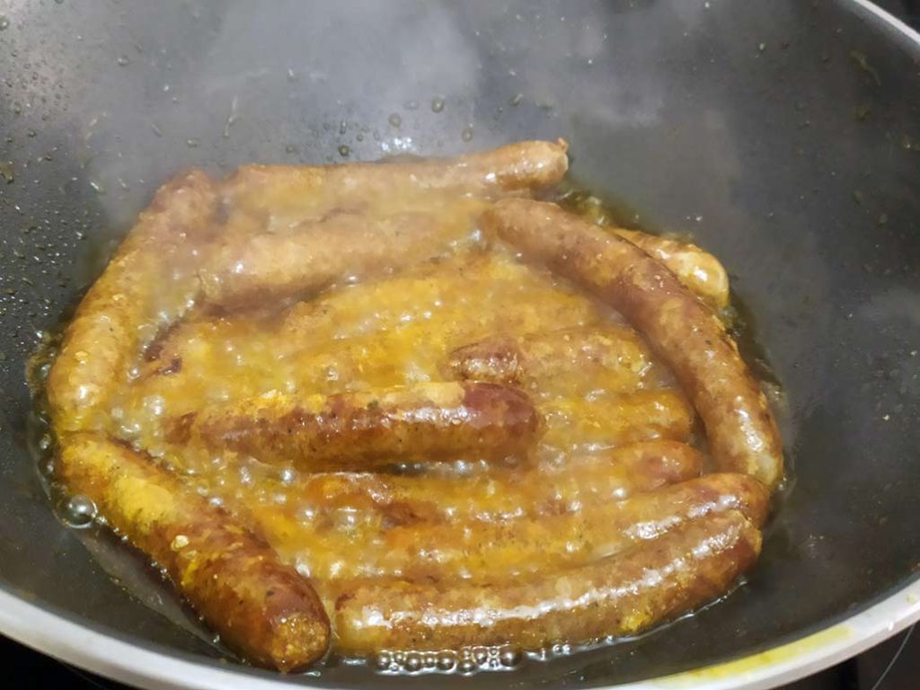 Merguez de cordero con aceite de oliva friéndose en una sartén tipo wok.